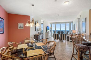 A spacious dining area with a glass table, wicker chairs, and a view of the ocean.