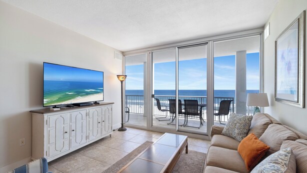 A living room with a TV, sofa, and a view of the ocean through large glass doors. - Island Tower 602 by Liquid Life (Gulf Shores)