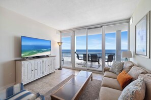 A living room with a TV, sofa, and a view of the ocean through large glass doors.