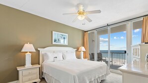 A bedroom with a large bed, two bedside lamps, a ceiling fan, a view of the ocean, and a balcony with chairs. - Island Tower 602 by Liquid Life (Gulf Shores)