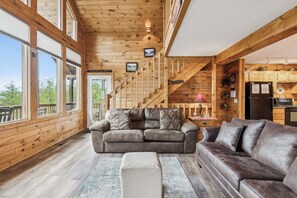 A wooden cabin interior with a sofa, ottoman, and a staircase leading to a loft.