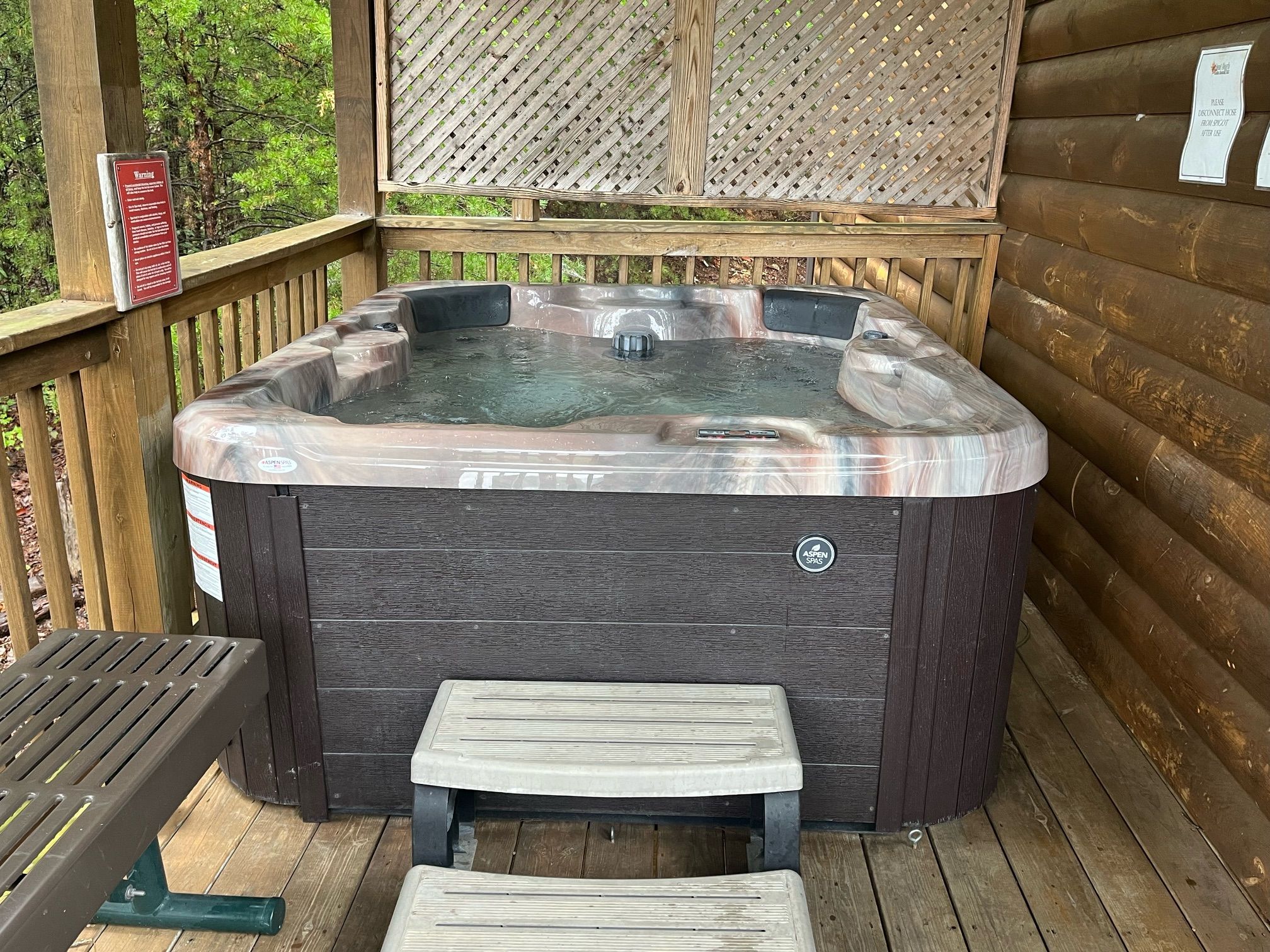 A hot tub on a wooden deck with a wooden fence and a warning sign.