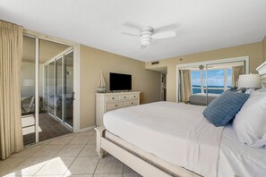 Ein Hotelzimmer mit einem großen Bett, einem Deckenventilator, einem Fernseher und Meerblick durch eine Schiebetür.