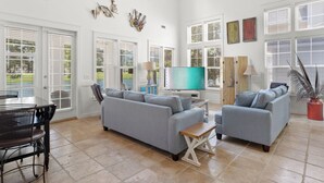 Ein geräumiges Wohnzimmer mit grauem Sofa, Fernseher und Essbereich mit Tisch und Stühlen.