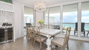 Zona pranzo con tavolo bianco, sedie in vimini, un lampadario e vista sull'oceano.