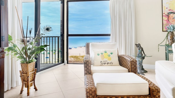 A room with a wicker sofa, a white cushion with a pineapple design, and a view of the beach through a large window. - ⭐Upgraded-Gulf Views-Walk2Beach-2 Pools+Hot Tub-2BR Mainsail 142⭐ (Miramar Beach)