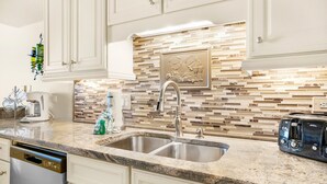 A kitchen with white cabinets, a granite countertop, a double sink, and a toaster. - ⭐Upgraded-Gulf Views-Walk2Beach-2 Pools+Hot Tub-2BR Mainsail 142⭐ (Miramar Beach)