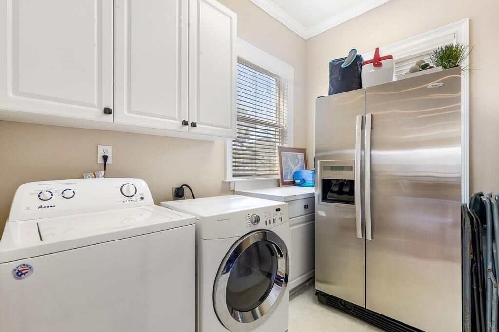 A laundry area with a front-loading washer and dryer, a stainless steel refrigerator, and white cabinetry.