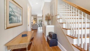 A hallway with a wooden bench, a table, and a staircase with white railings. - Family Fun Beach House! Ocean Views, Private Pool, Fire Pit, Video Games, Pool Table, Elevator! (Isle of Palms)