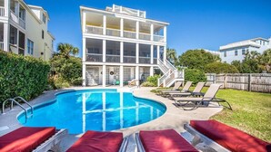 A swimming pool with lounge chairs and a multi-story building with balconies. - Family Fun Beach House! Ocean Views, Private Pool, Fire Pit, Video Games, Pool Table, Elevator! (Isle of Palms)