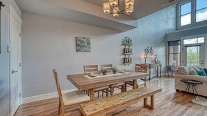 A dining area with a wooden table, benches, and chairs. There is a chandelier above the table, and a bicycle is visible in the background. - Highside Condo @ The River Lofts ~ New condo on the Arkansas River (Salida)