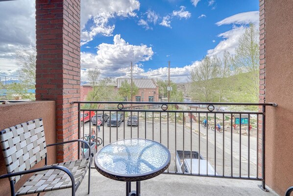 A balcony with a metal railing, a woven chair, and a glass table.