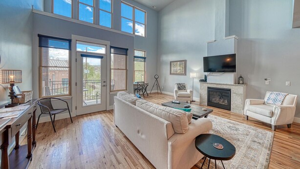 A spacious living room with a fireplace, a large TV, and a balcony with a view. - Highside Condo @ The River Lofts ~ New condo on the Arkansas River (Salida)