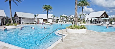 A swimming pool area with multiple pools, palm trees, and buildings with white roofs.