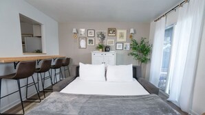 A modern hotel room with a bed, a desk, chairs, a wardrobe, and a window with curtains. - Riverfront Oasis| Pool | King Bed Walk to Broadway (Nashville)