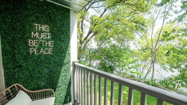 A balcony with a green wall and a wicker chair, overlooking a body of water. - Riverfront Oasis| Pool | King Bed Walk to Broadway (Nashville)