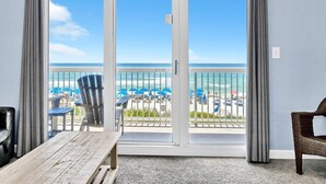 Une pièce avec une table en bois, une chaise en osier et une vue sur la plage, visible à travers une porte-fenêtre coulissante.