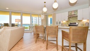Een moderne keuken met witte kasten, een centraal eiland en een eetgedeelte met rieten stoelen.
