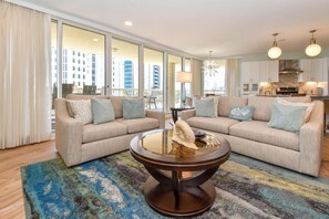 A modern living room with two sofas, a glass coffee table, and a view of the cityscape through large windows.
