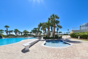 Een zwembad met terras, palmbomen en een gebouw op de achtergrond.