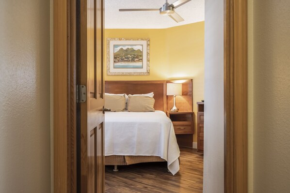 Una habitación de hotel con cama, mesita de noche, lámpara y ventilador de techo.