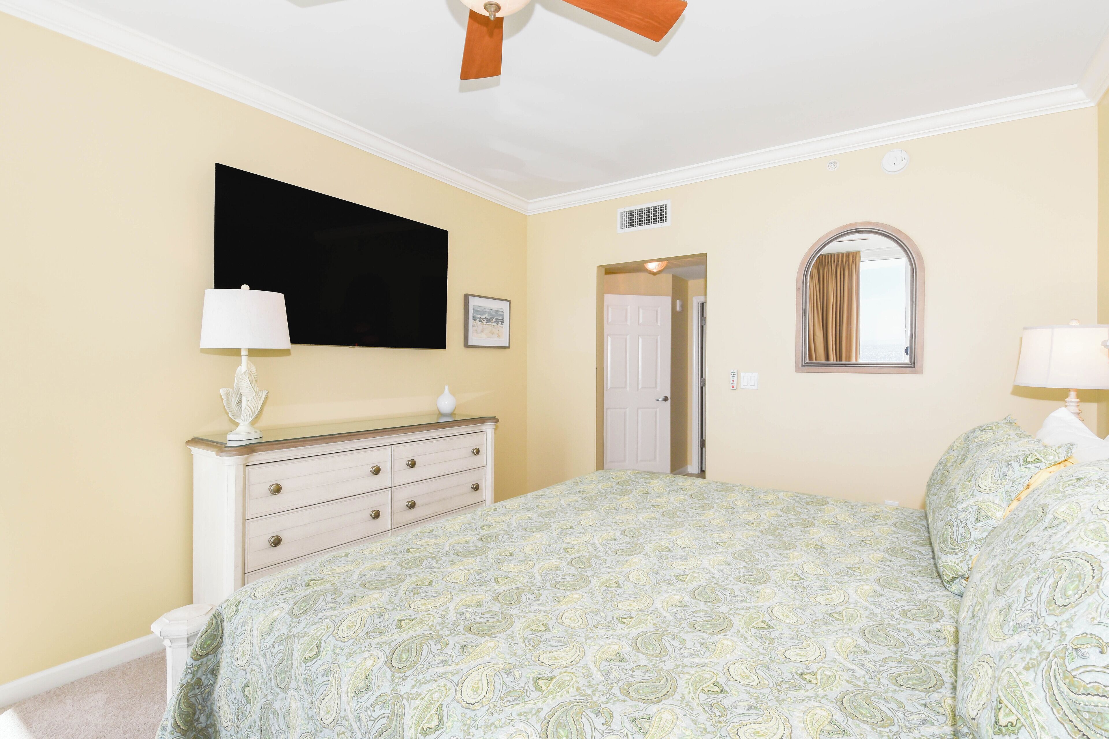 A bedroom with a bed, dresser, and a flat-screen TV on the wall.
