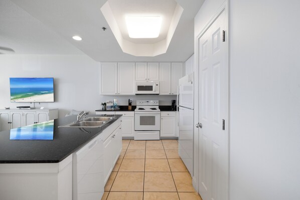 A modern kitchen with white cabinets, a black countertop, a microwave, an oven, and a sink.