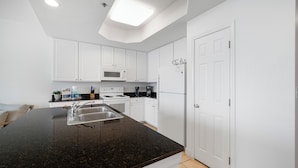 A modern kitchen with white cabinets, a granite countertop, a microwave, a stove, and a refrigerator. - Lighthouse 304 by Liquid Life (Gulf Shores)