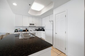 A modern kitchen with white cabinets, a granite countertop, a microwave, a stove, and a refrigerator.