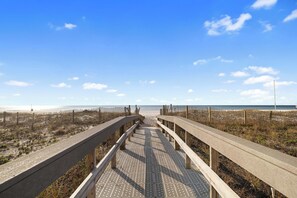 A wooden boardwalk leading to a beach with a clear sky.