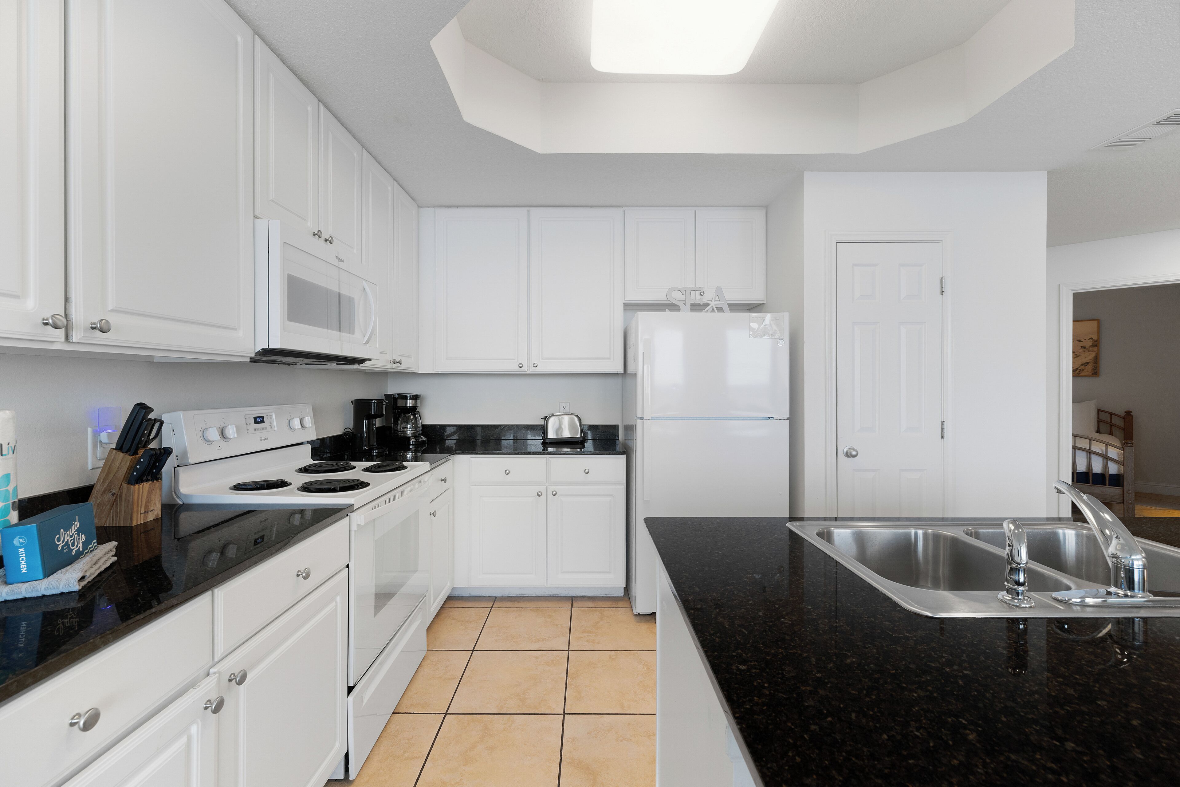 A modern kitchen with white cabinets, a black countertop, stainless steel sink, and a refrigerator.
