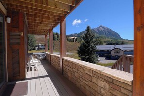A wooden deck with a stone wall, overlooking a mountain and a residential area.