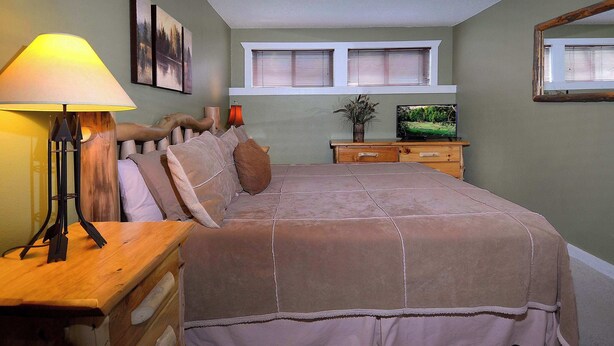 Ein Schlafzimmer mit einem Bett, Nachttischen, einer Lampe, einem Fernseher und einem Fenster mit Jalousien.
