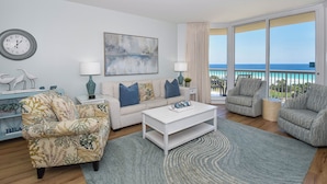 A living room with a sofa, armchairs, a coffee table, a clock, and a painting. - Charming, bright beachfront condo w/private balcony! 🌴 (Destin)