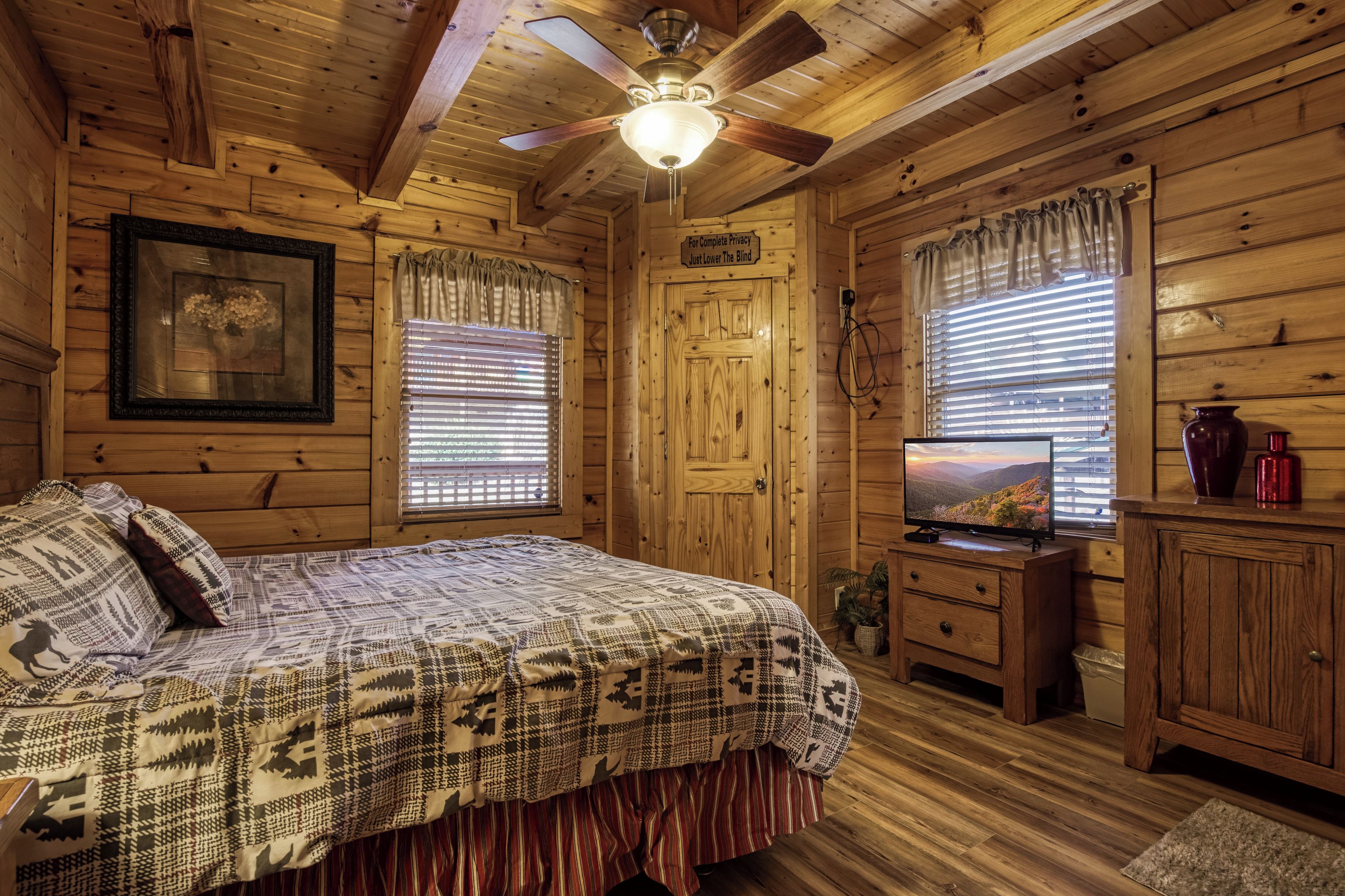 Une chambre dans une cabane en bois, avec un lit, une télévision et une fenêtre équipée de stores.