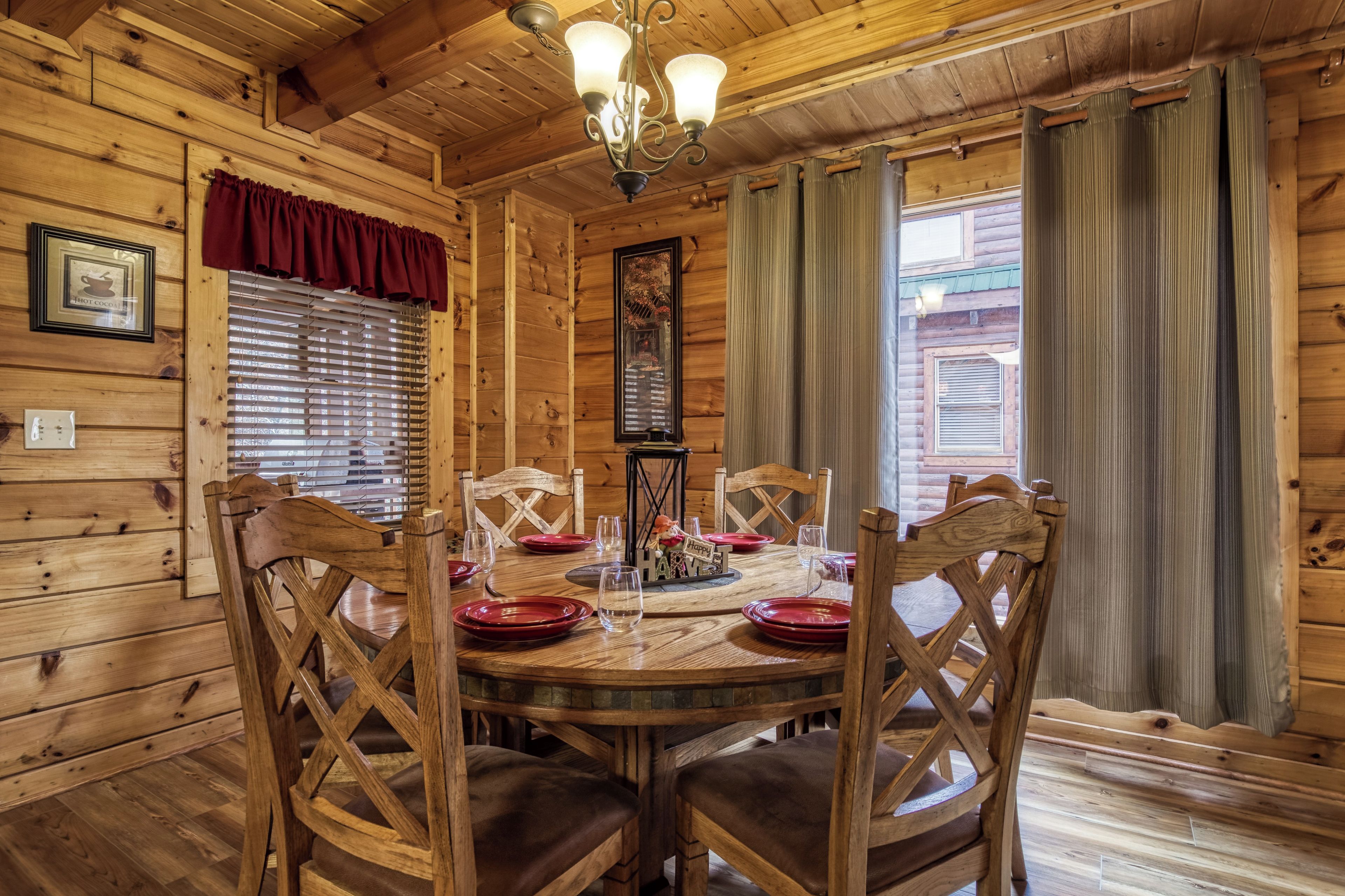A wooden dining room with a round table, chairs, and a chandelier.