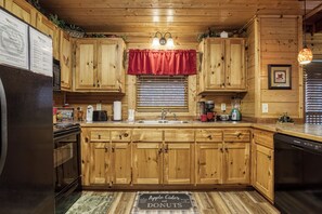 A wooden kitchen with a red valance, a sink, and various appliances including a coffee maker and a kettle.