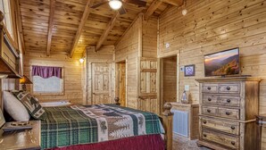 Une chambre située dans un chalet en rondins, avec un lit, une commode et un téléviseur diffusant des images d’un paysage pittoresque.
