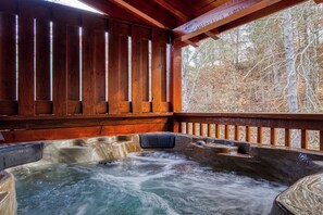 A wooden cabin with a hot tub and a view of a forest.