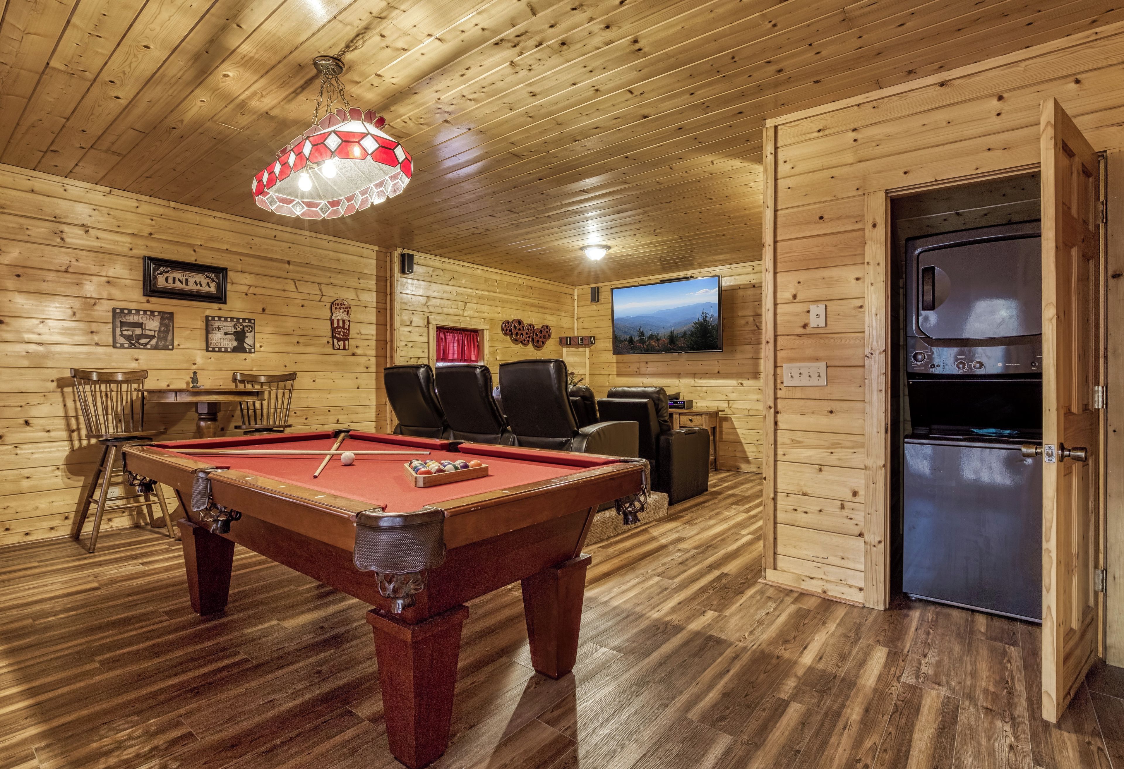 A wooden interior with a pool table, chairs, a television, and a refrigerator.