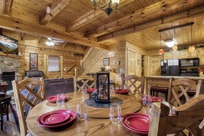 A wooden cabin interior with a dining area, kitchen, and a fireplace.