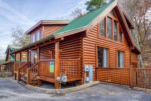 A log cabin with a porch, a staircase, and a view of the surrounding forest.