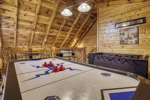 Une pièce au plancher de bois, équipée d’un baby-foot, d’un coin bar et d’une enseigne fixée au mur indiquant qu’il s’agit d’une « PIÈCE POUR FILLES ».