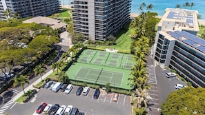 Un hotel de varios pisos con cancha de tenis, estacionamiento y vista al océano.