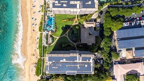Un hotel sulla costa con pannelli solari, una spiaggia e un campo da tennis.