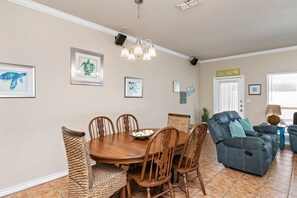 A dining area with a wooden table and chairs, a blue sofa, and wall art including a turtle and a seahorse.