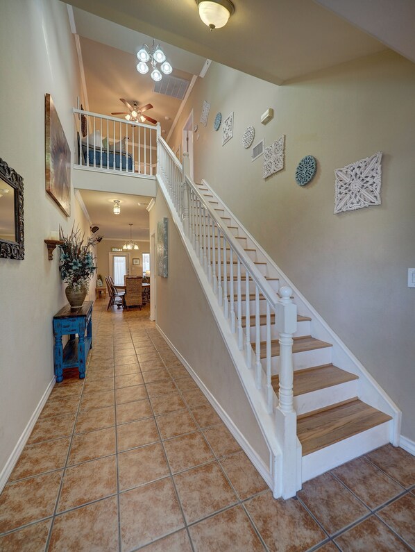 A spacious hallway with a white staircase, a ceiling fan, and decorative wall art.