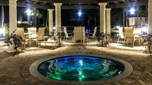 Zona de piscina exterior con una piscina circular, rodeada de columnas y sillas blancas.