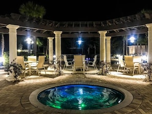 Area piscina esterna di notte, con piscina circolare, colonne bianche e poltrone relax.