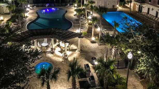 Un área de piscina exterior bien iluminada con sillones de descanso y una zona de estar cubierta.